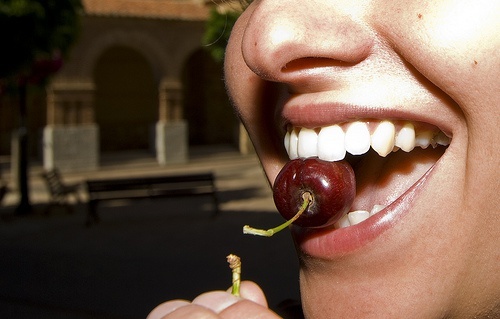 Mulher comendo uma cereja, pois não range os dentes
