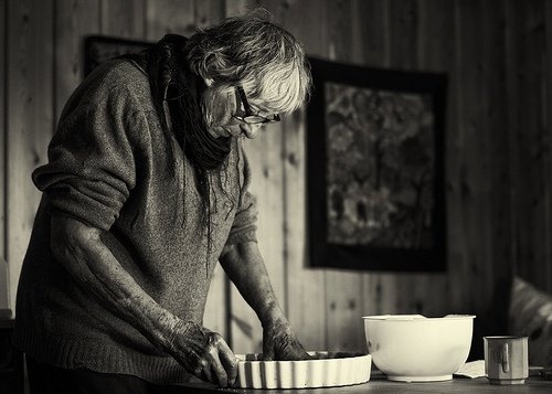 Mulher idosa fazendo comida cansada devido a Síndrome do cuidador