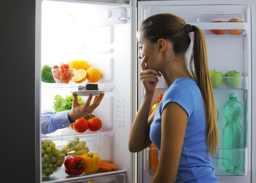Mulher olhando para a geladeira pensando em quebrar suas dietas