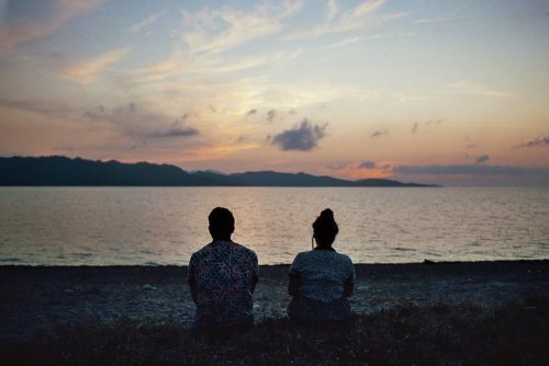 Casal observando o reflexo do por do sol na água