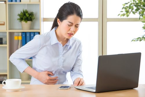 Mulher ao computador com dor de barriga