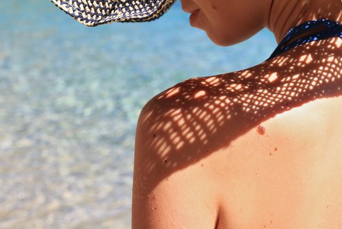 Mulher de costas na praia com chapéu para combater o calor