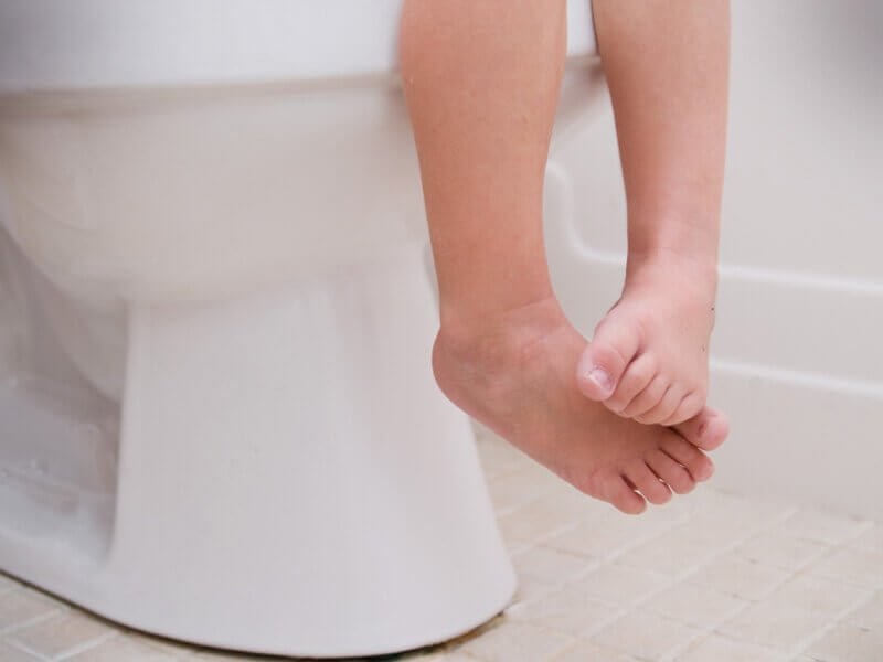 Pés de criança sentada no vaso sanitário