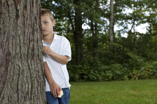 Menino com Síndrome de Asperger se escondendo atrás de árvore