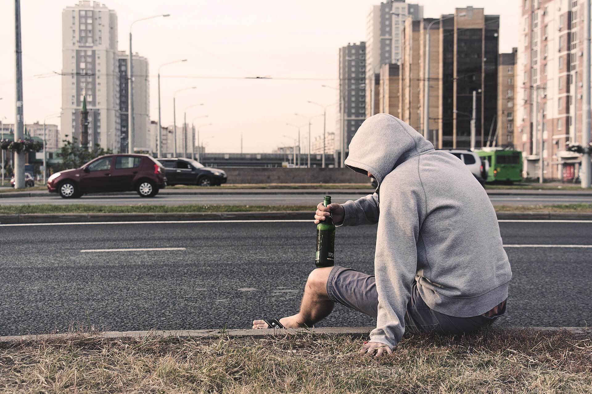 Homem com garrafa bebendo álcool no meio-fio