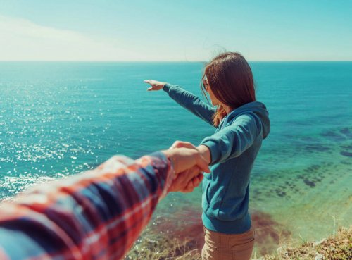 Mulher olhando para o mar segurando da mão de um homem