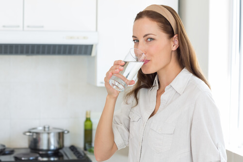 Mulher bebendo água em sua cozinha