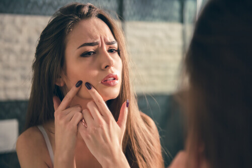 Mulher se olhando no espelho, procurando por acne