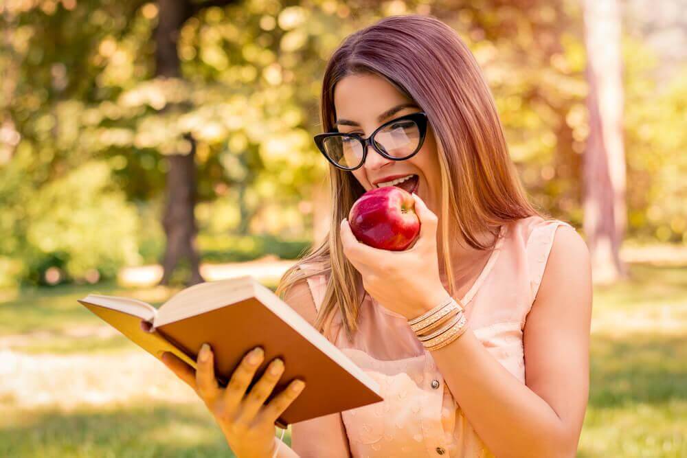 Mulher lendo livro e comendo maçã
