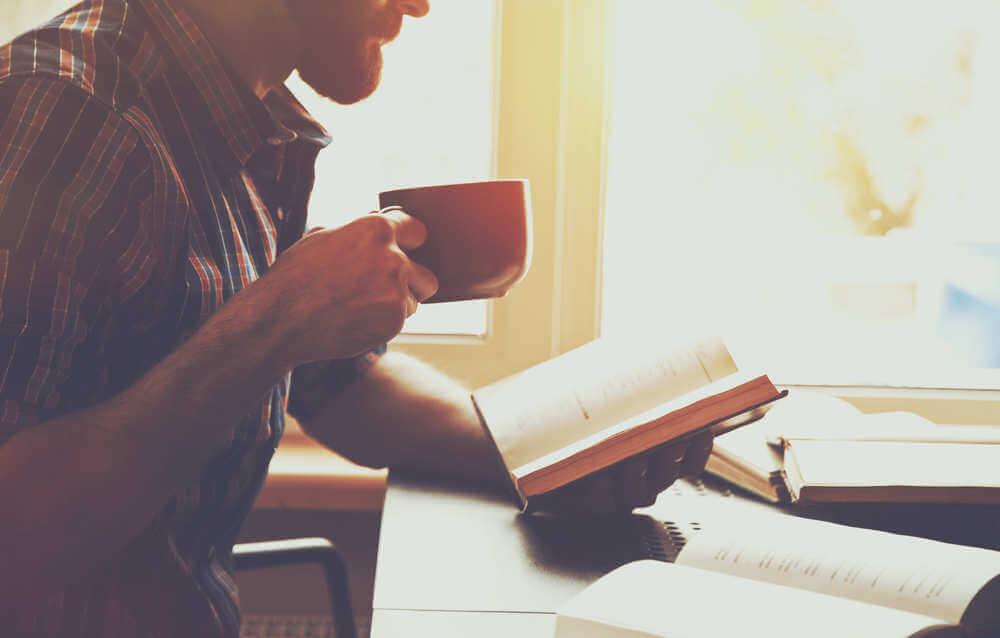 Homem lendo livro com xícara de café