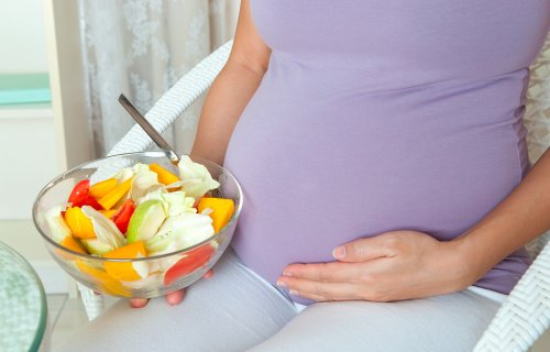 Mulher grávida segurando tigela de frutas