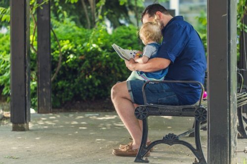 Pai ensinando uma criança a ler no parque.