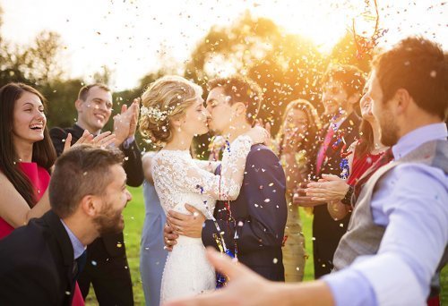 Casal de noivos beijando no casamento com padrinhos e parentes