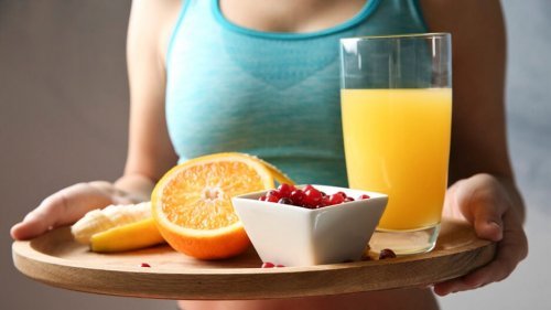 Mulher carregando uma bandeja de comida com suco, laranjas e uma tigela com frutas após o exercício.